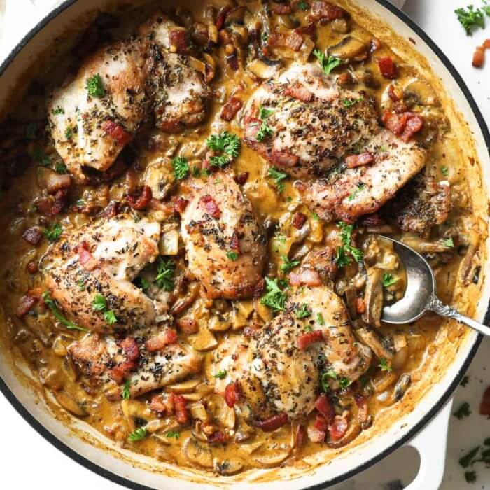 Vertical overhead image of skillet full of garlicky chicken in a creamy sauce with bacon.