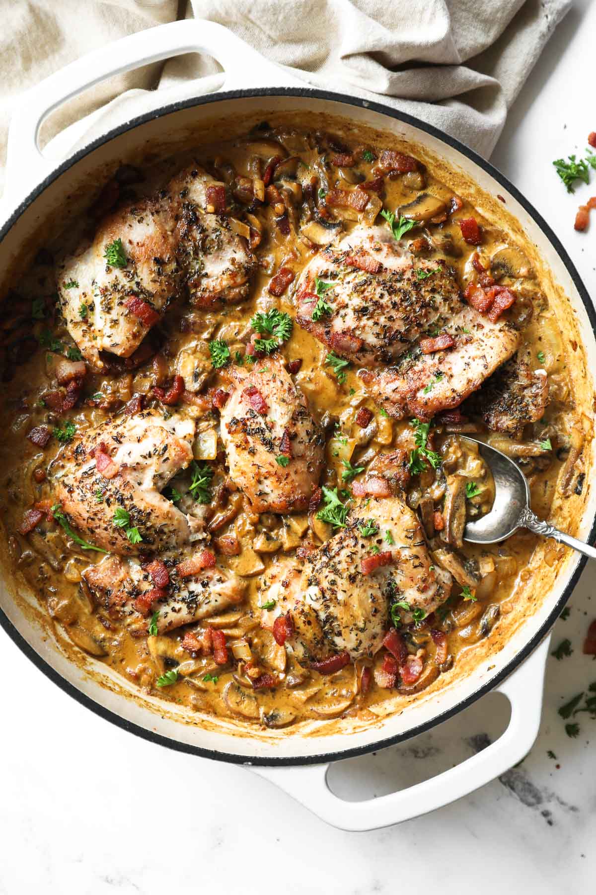 Vertical overhead image of skillet full of garlicky chicken in a creamy sauce with bacon.