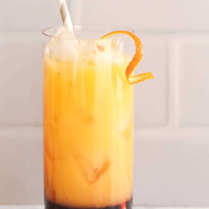 Orange sunrise mocktail in a jar with a straw coming out and orange peel garnish.