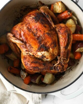 Close up overhead image of dutch oven filled with cooked veggies and a whole chicken.