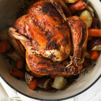 Close up overhead image of dutch oven filled with cooked veggies and a whole chicken.