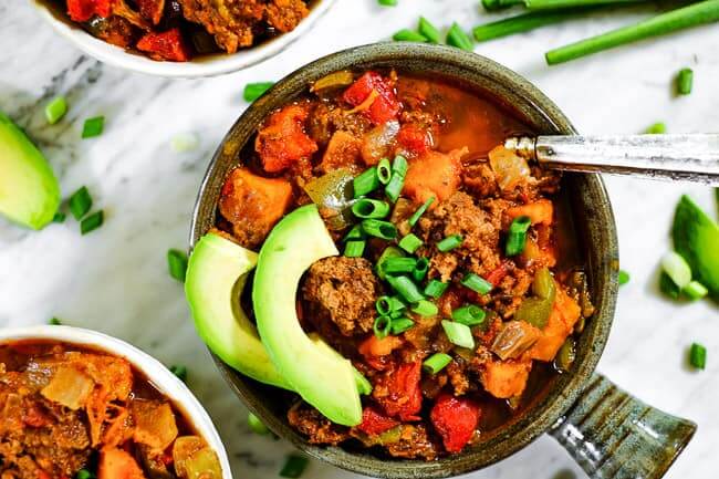 Paleo + Whole30 sweet potato chili served up in bowls with chopped green onion and avocado slices. 