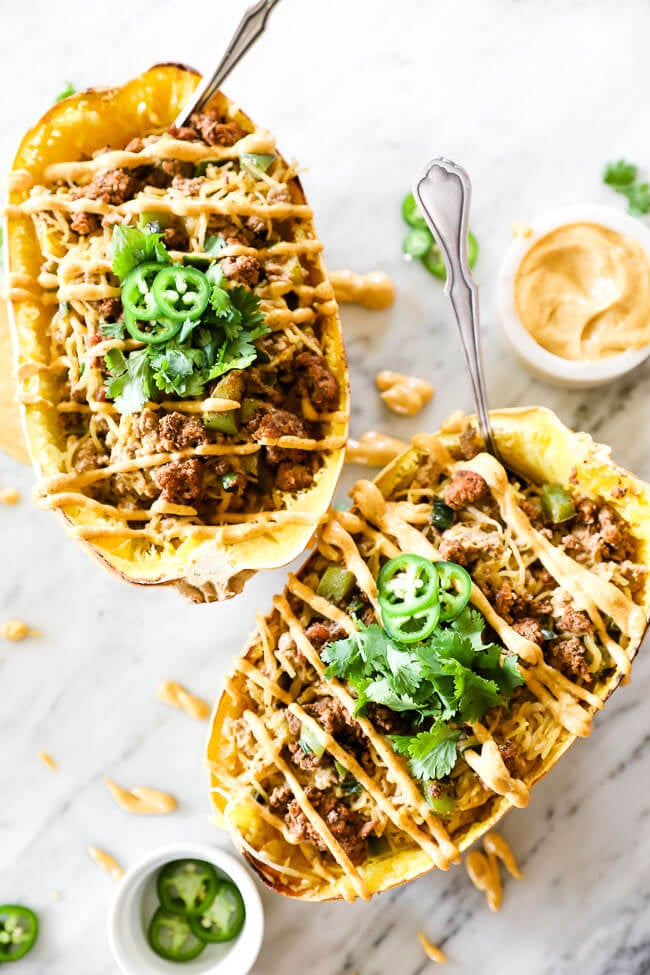 Two taco stuffed spaghetti squash with sauce drizzled on top and spoons coming out of the squash