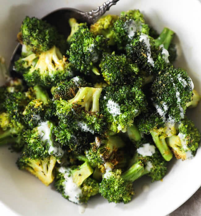 Overhead image of air fryer broccoli in a bowl with ranch drizzled on top and serving spoon in the dish.