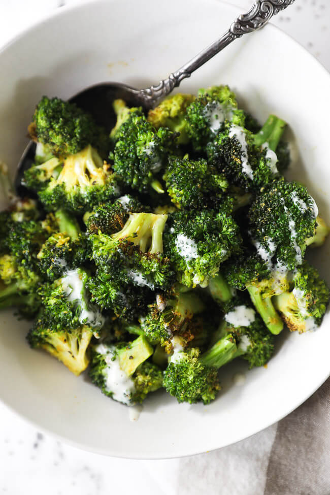 Overhead image of air fryer broccoli in a bowl with ranch drizzled on top and serving spoon in the dish.