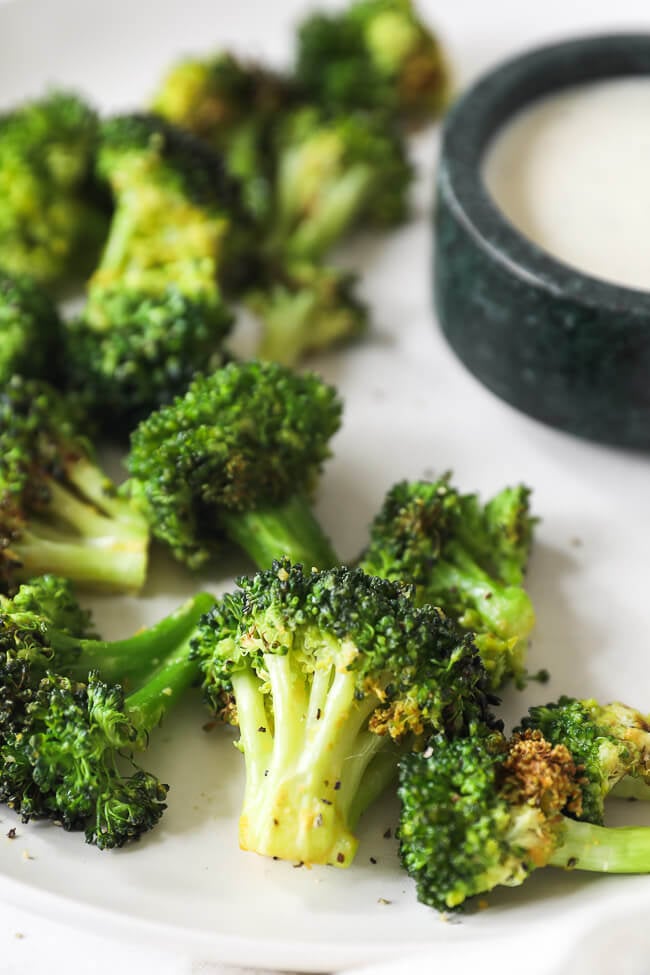 Angled close up of air fryer broccoli on a plate with ranch sauce in the background.