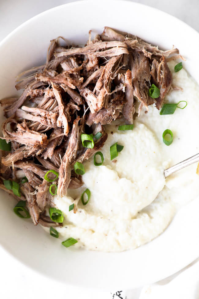 Close up of pulled pork over mashed cauliflower in a bowl with chopped green onion on top. 