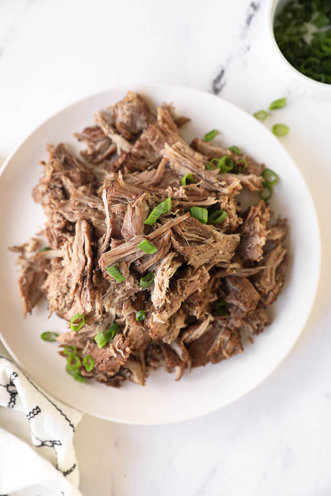 Overhead image of instant pot pulled pork piled on a plate with with chopped green onion on top. 