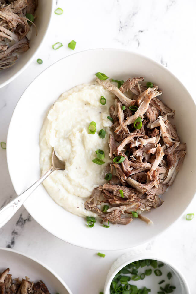 Bowl of mashed cauliflower and instant pot pork shoulder, topped with chopped green onion. 