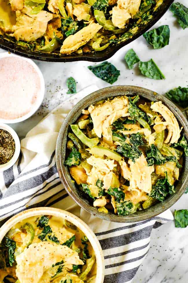 Thai coconut curry served in a bowl with extra skillet and a second bowl. Extra salt, pepper and kale on the table. 
