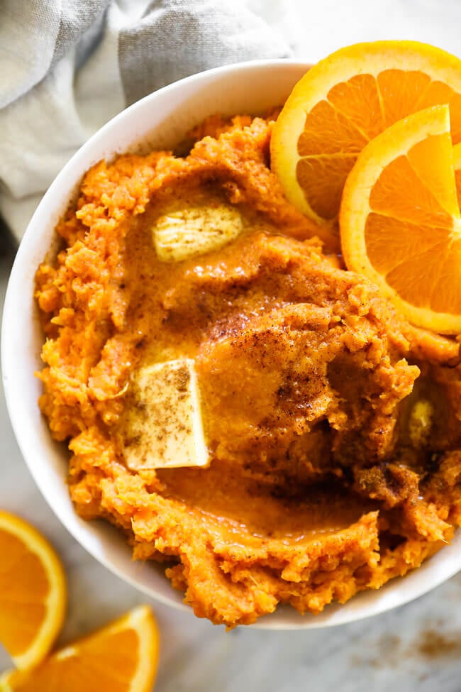 Close up overhead vertical image of Thanksgiving yams in a bowl with melted butter and cinnamon on top. 