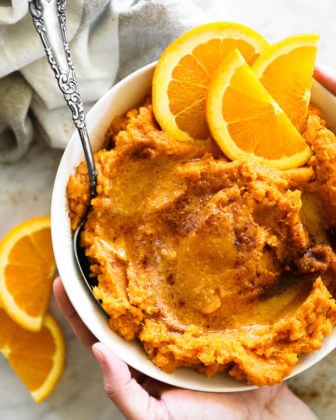 Mashed thanksgiving yams in a bowl with orange wedges