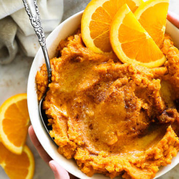 Mashed thanksgiving yams in a bowl with orange wedges