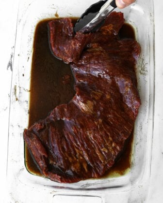 Tong holding skirt steak in a balsamic marinade