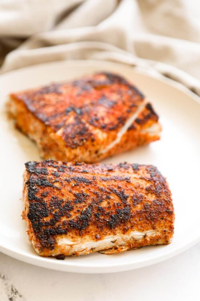 Angled image of two pieces of blackened mahi mahi on a plate. The piece in the front is in focus while the other piece is blurry in the background.