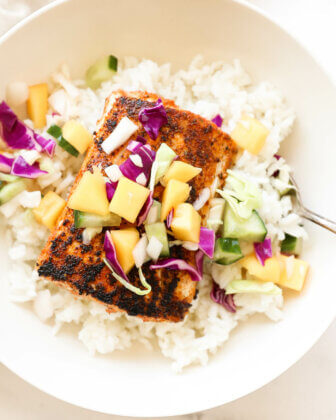 Close up shot of blackened mahi mahi in a bowl over rice and topped with mango slaw.
