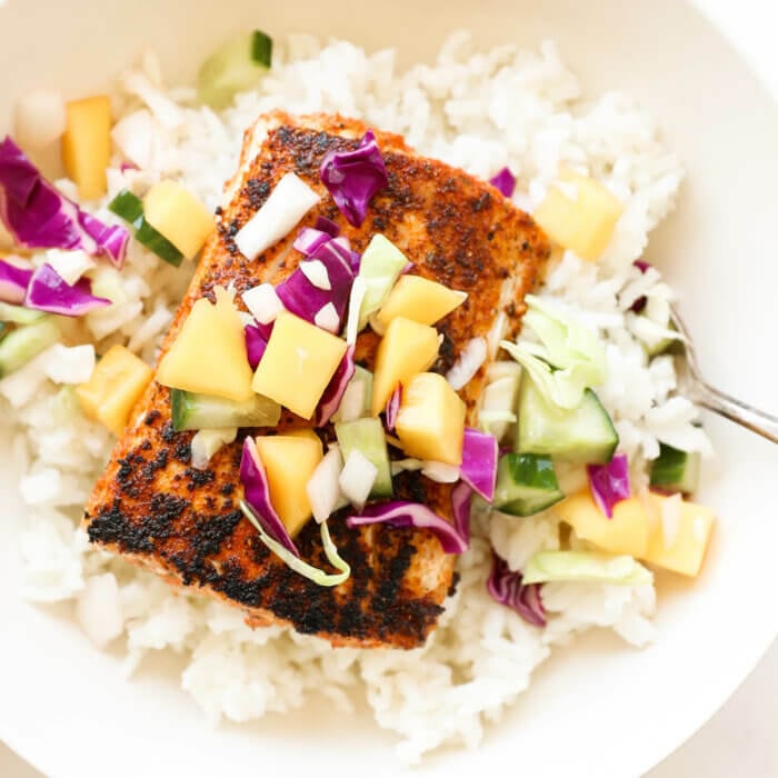 Close up shot of blackened mahi mahi in a bowl over rice and topped with mango slaw.