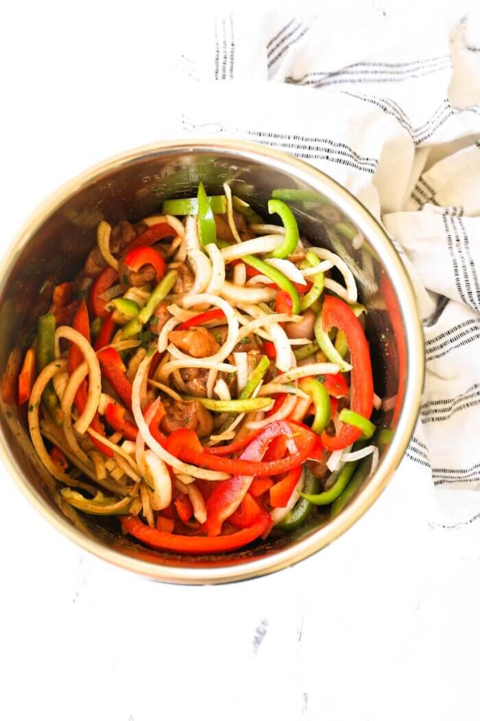 Overhead shot of instant pot before cooking, filled with cut up pieces of chicken, sliced red and green bell peppers, onion and a flavorful marinade sauce.