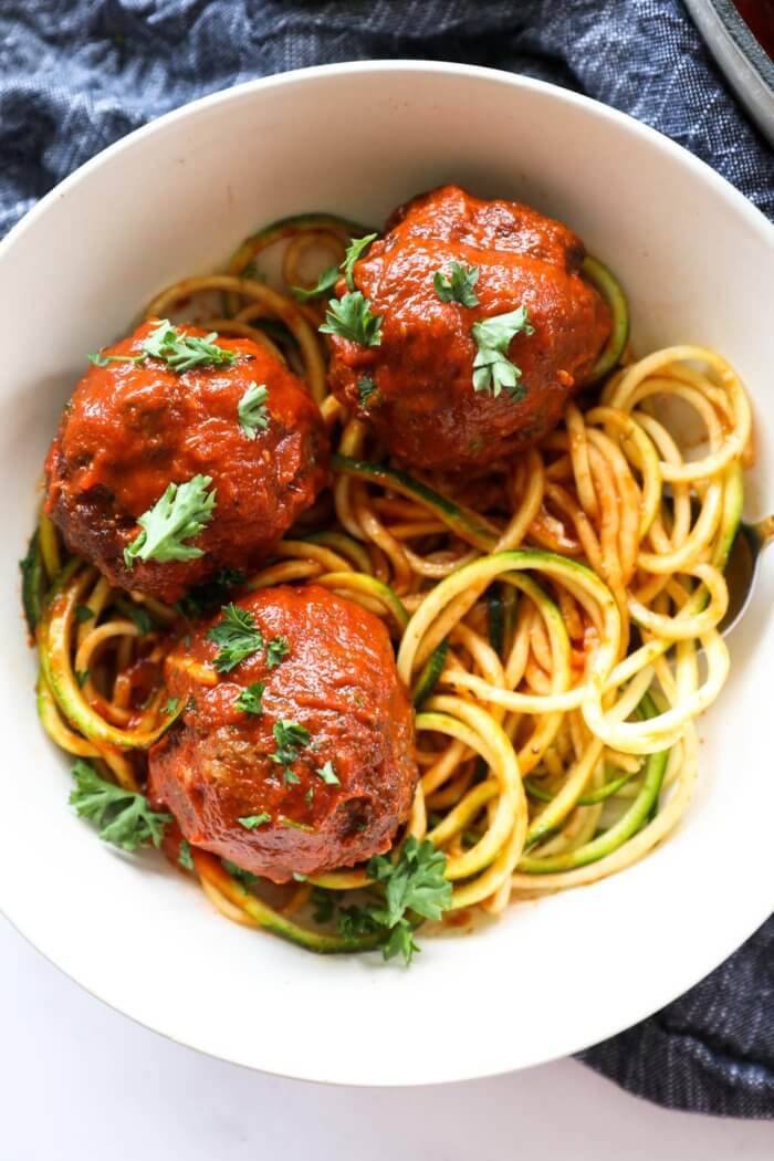 Close up overhead image of a bowl of zoodles topped with 3 big meatballs and marinara sauce. Fresh chopped parsley sprinkled on top.