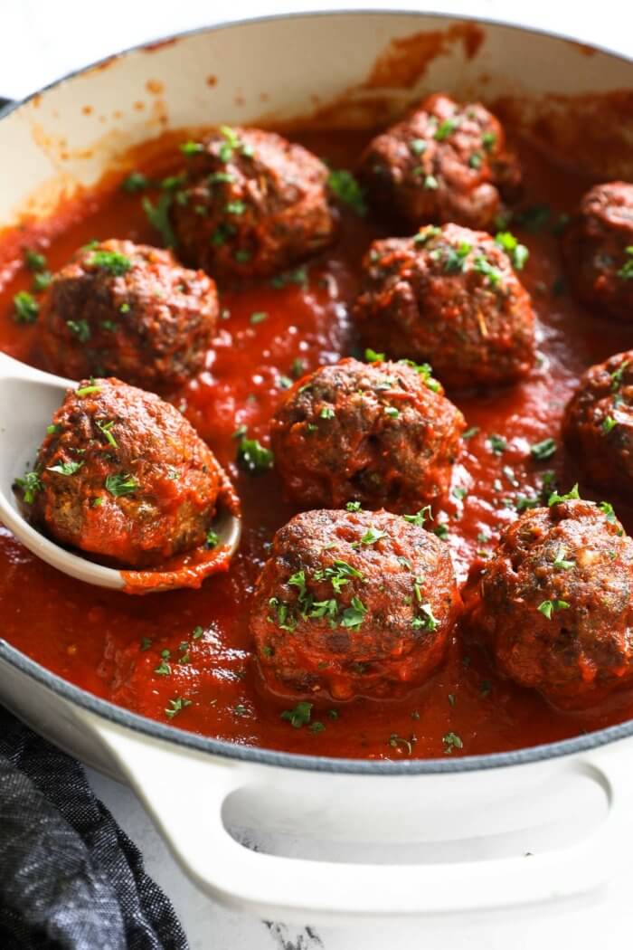 Angled image of meatballs simmering in skillet with a serving spoon scooping up one meatball.