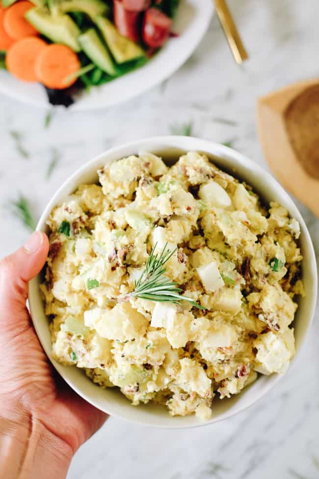 Holding the best potato salad with bacon in a bowl with rosemary