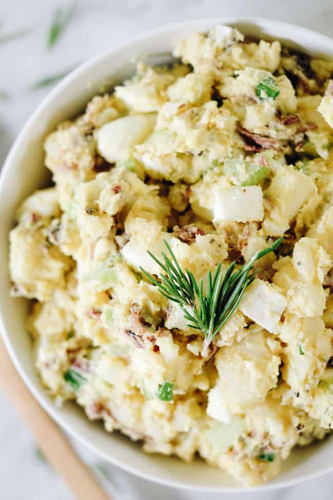 Close up shot of the best potato salad with bacon in a bowl with rosemary