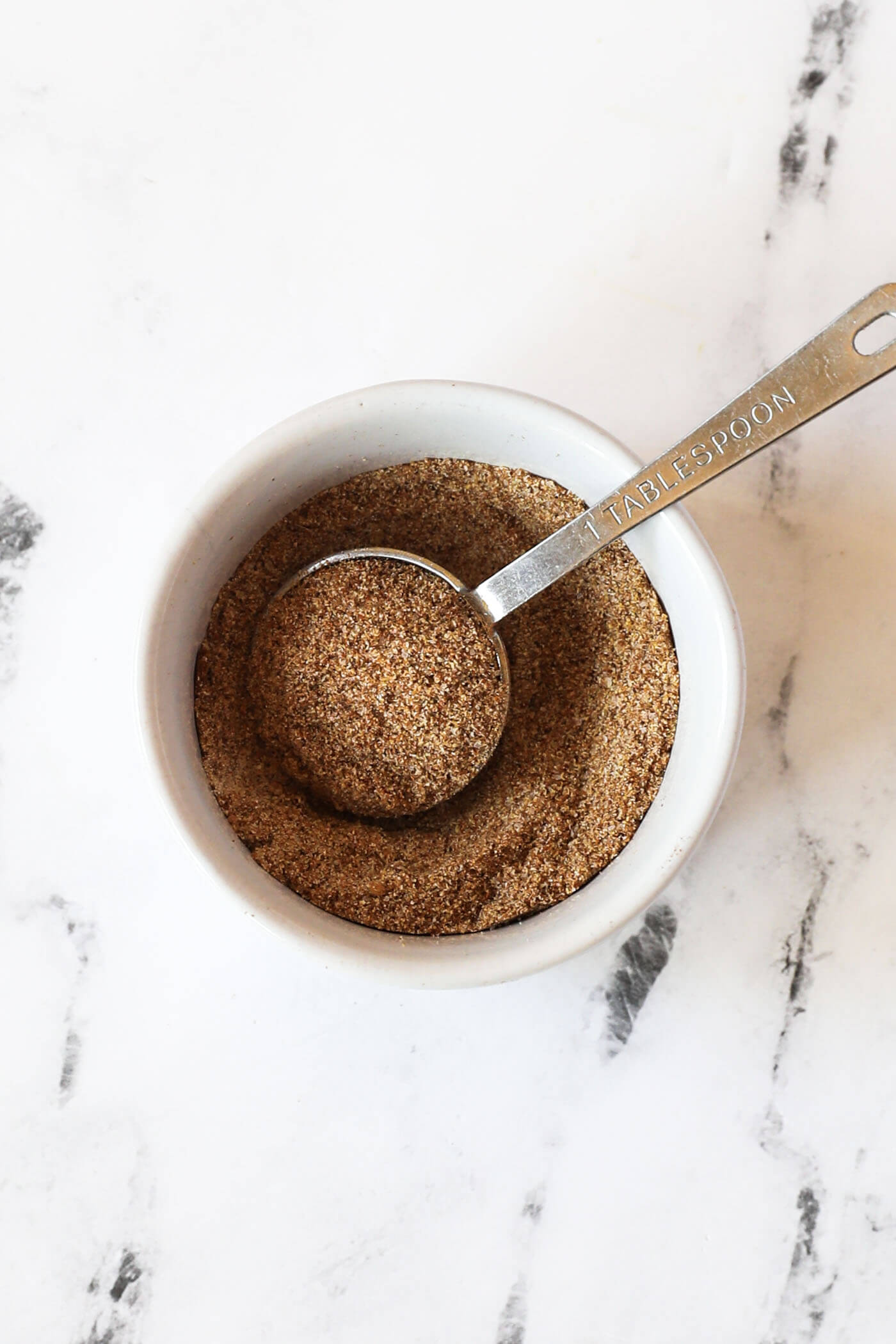 Dry rub ingredients for smoked pulled pork in a ramekin with a measuring spoon.