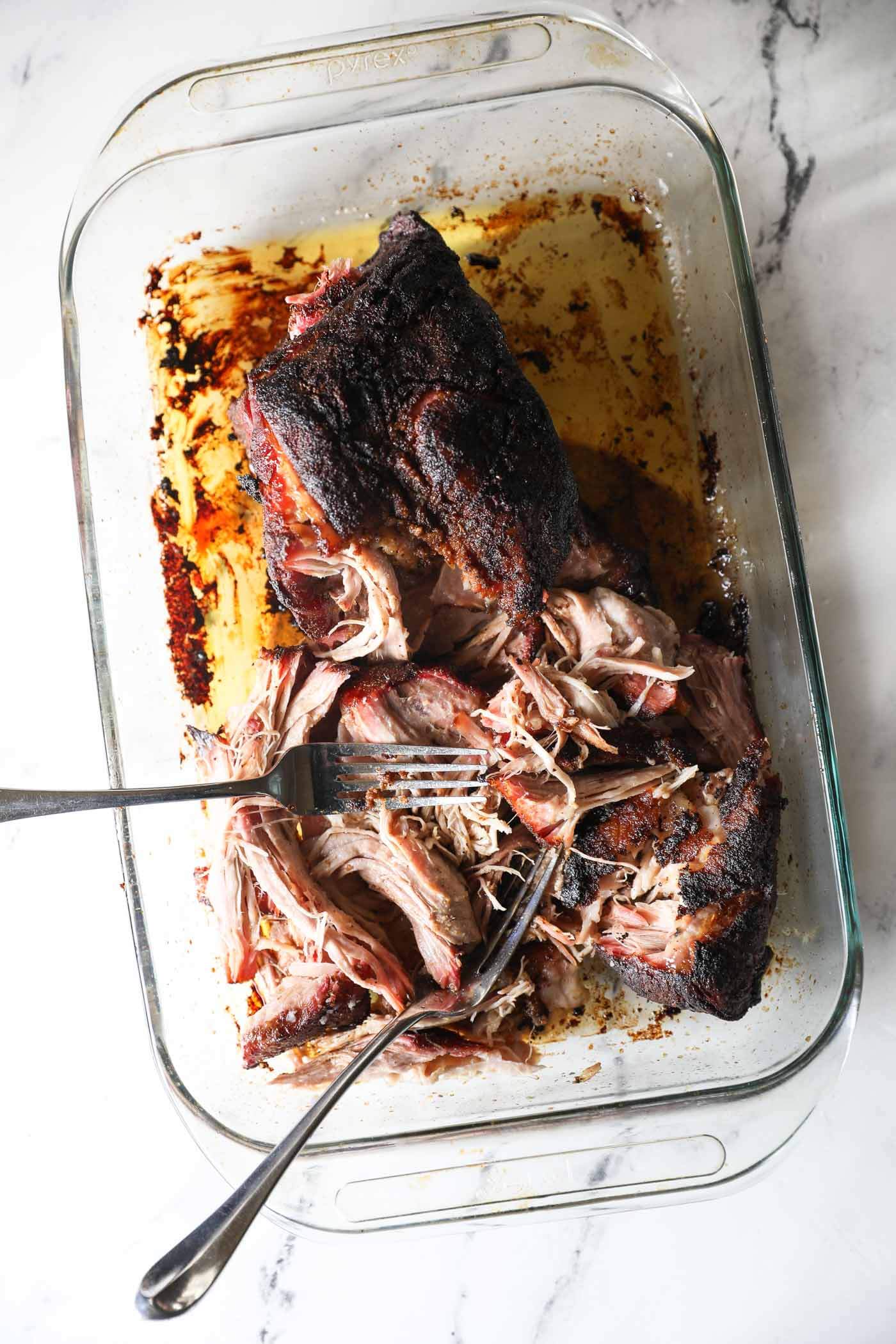 Shredded pork after the roast is pulled off the grill. The two forks are still in the pan.
