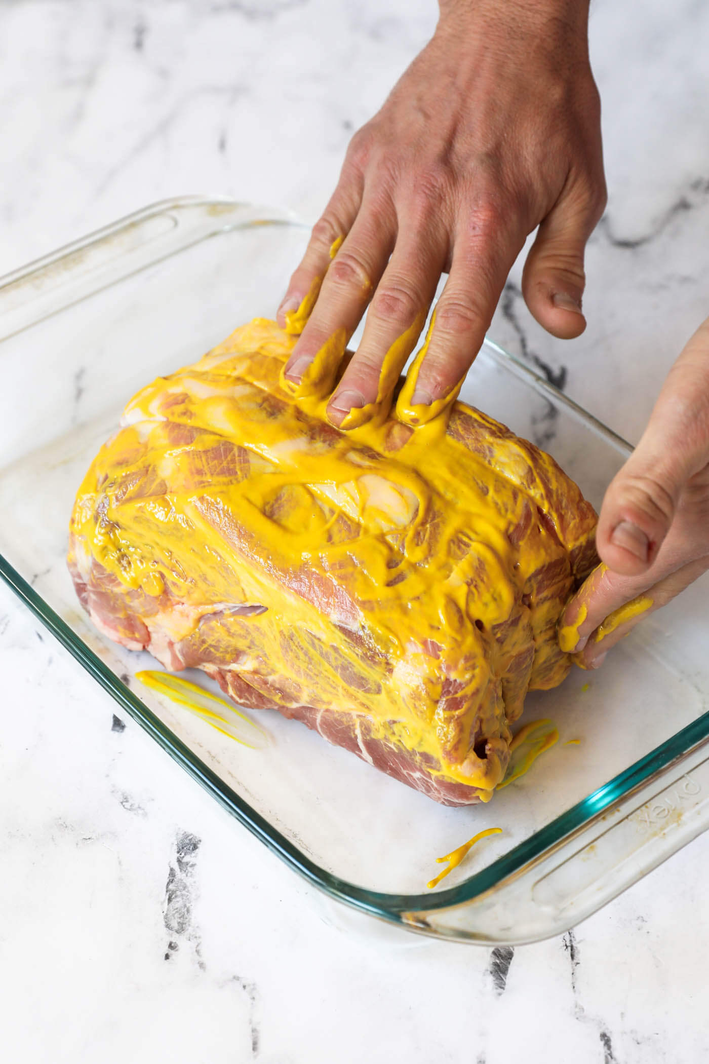 A had spreading yellow mustard all over a raw pork butt before sprinkling on the dry rub.