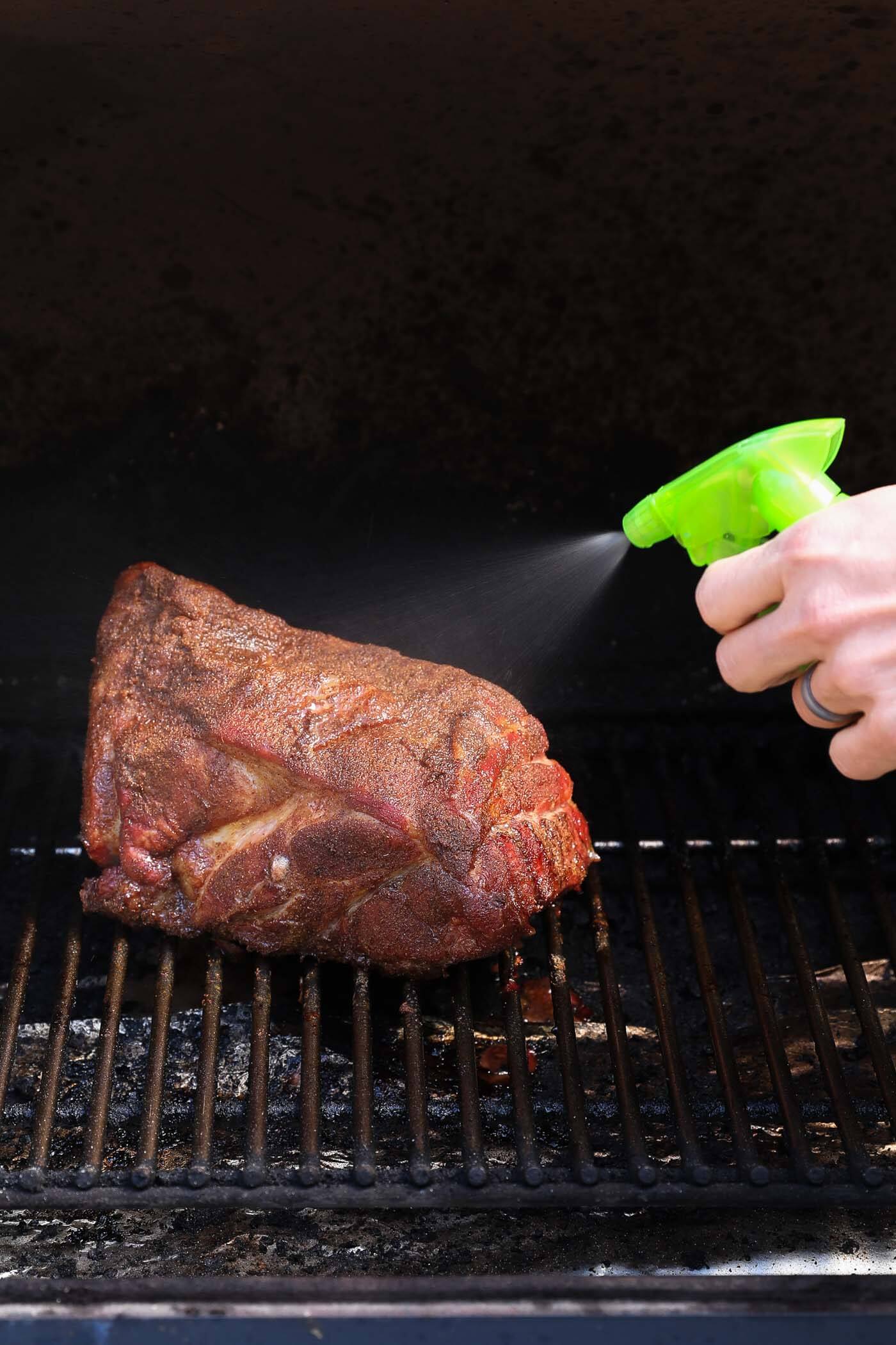 Pork butt roast cooking on a traeger grill and someone is spraying apple juice on it as it cooks.
