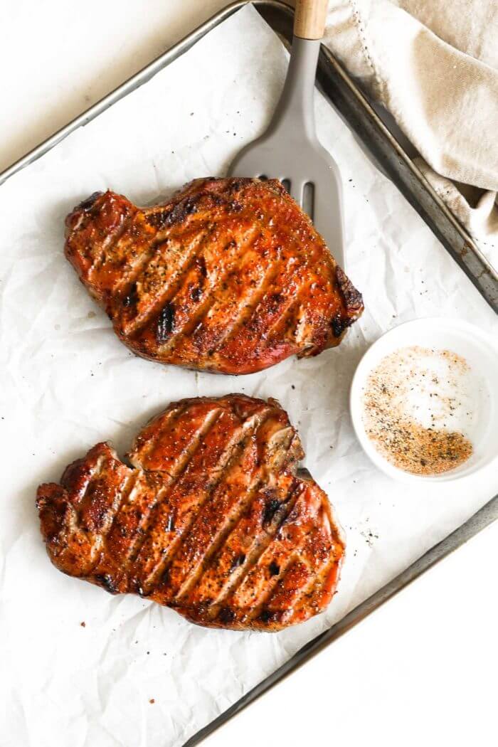 Overhead shot of traeger smoked pork chops on a pan with seasoning and spatula under one chop