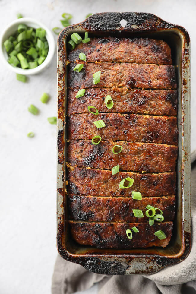 Chicken meatloaf sliced in a loaf pan with green onion on top
