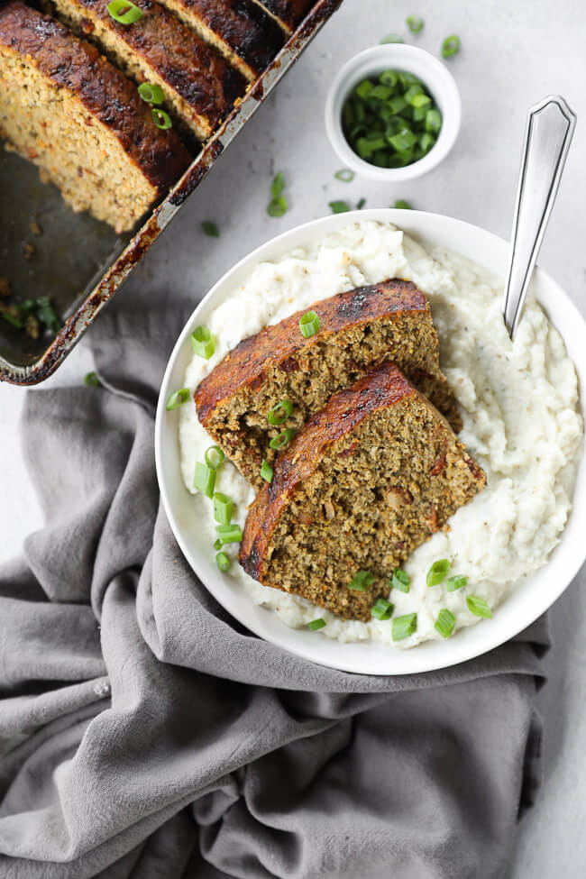 Two slices of chicken meatloaf over a bowl filled with mashed potatoes and a spoon coming out