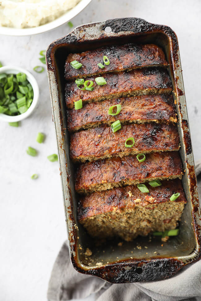 Overhead image of chicken meatloaf sliced in a loaf pan with green onion on top