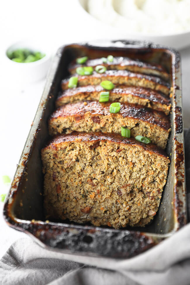 Close up angle image of chicken meatloaf slices in a loaf pan with green onion on top