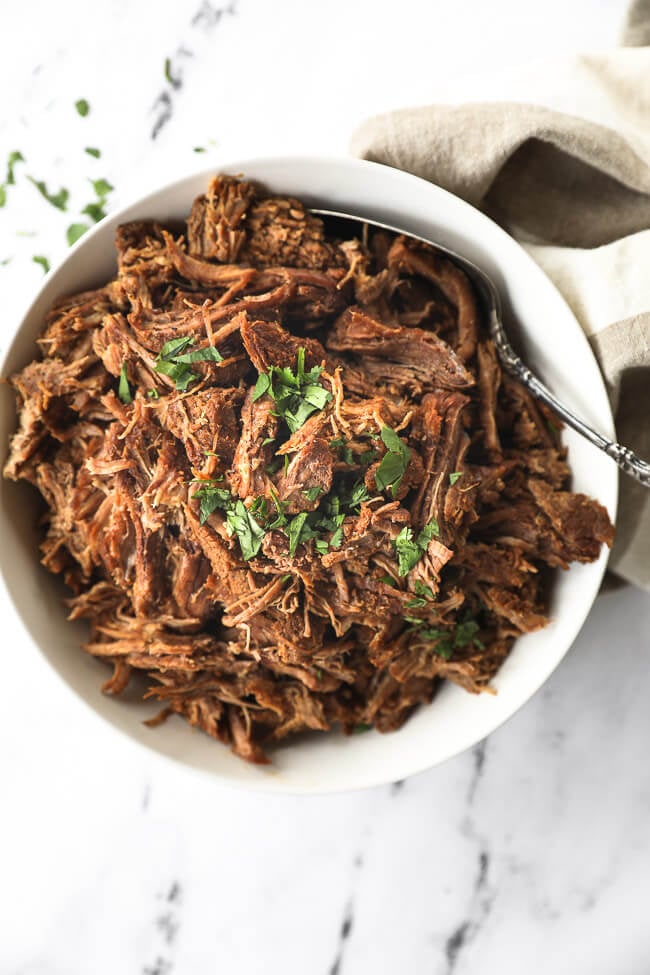 Instant pot shredded beef in a white bowl with chopped parsley topping