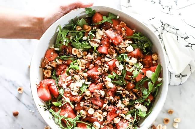 Overhead horizontal image of watermelon salad in a large serving bowl. Watermelon, arugula, hazelnuts, balsamic vinegar and optional feta cheese. 