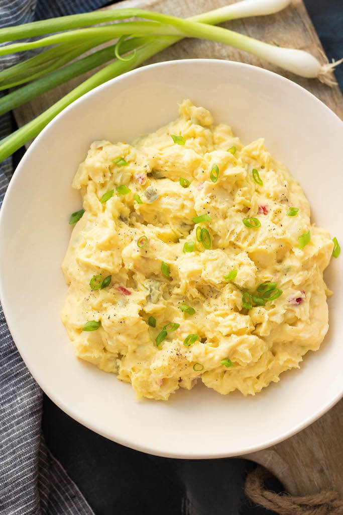 Mustard potato salad in a white bowl with diced green onions on top