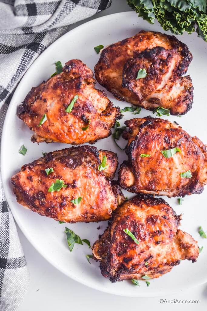 Overhead image of air fryer chicken thighs on a white plate with chopped green garnish sprinkled on top