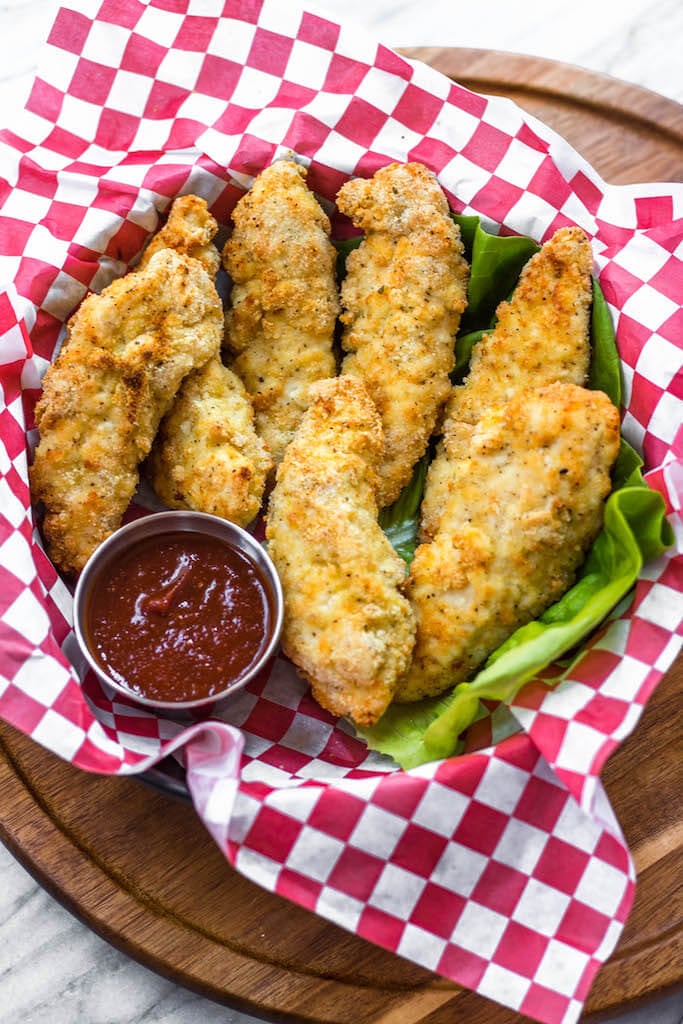 Chicken tenders in a red plaid basket with ketchup on the side
