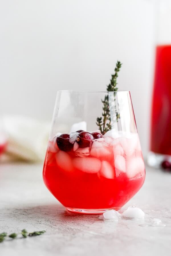 Red iced holiday punch in a glass with cranberry and thyme garnish