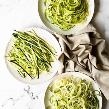 Overhead image of zucchini noodles on three separate plates. One made from standup spiralizer, one from a handheld spiralizer and one from a veggie peeler.