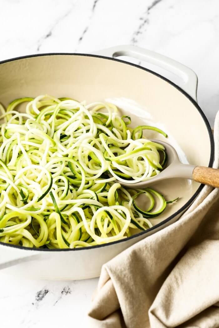 Angled image of zucchini noodles in a skillet with a serving spoon.