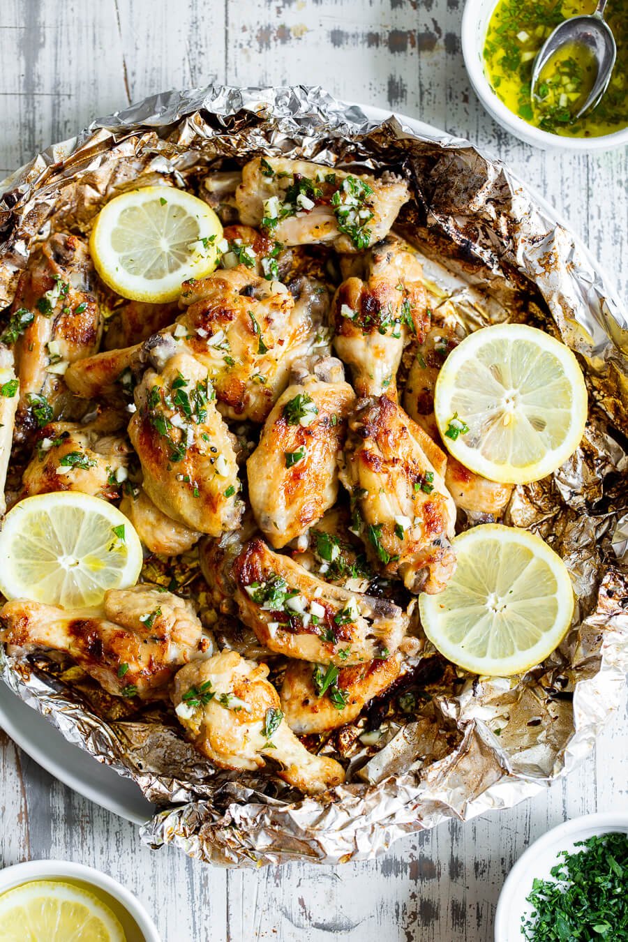 Plate of grilled wings with lemon wedges and chopped herbs