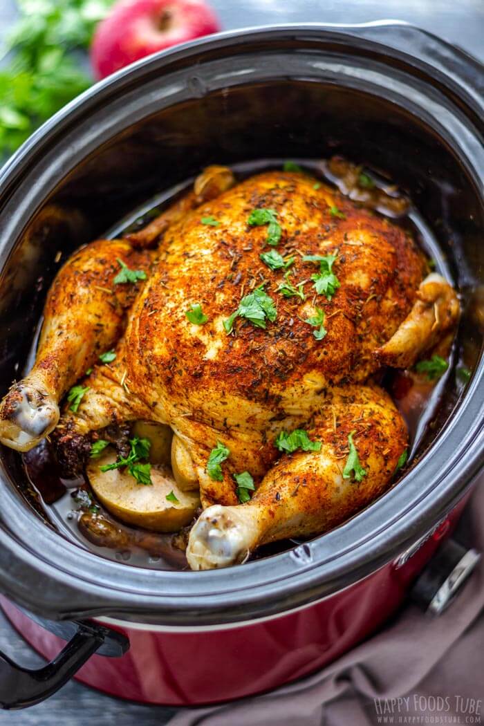 Whole cooked chicken in a crockpot with seasonings spread over it and chopped parsley flakes